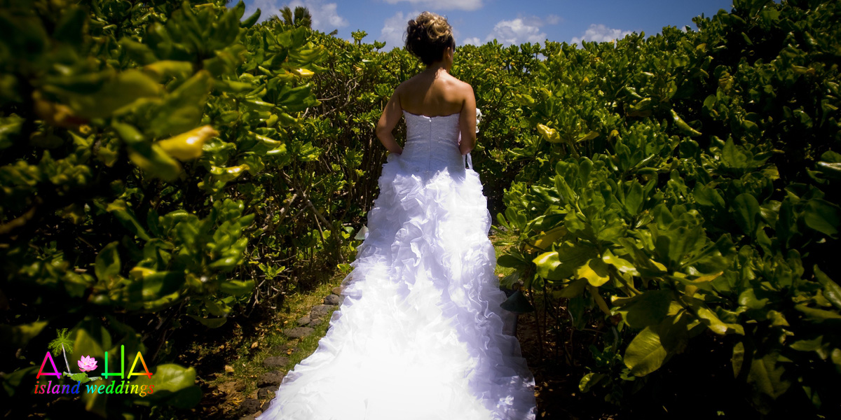 Bride walking along a path through green bushes toward her beach ceremony
